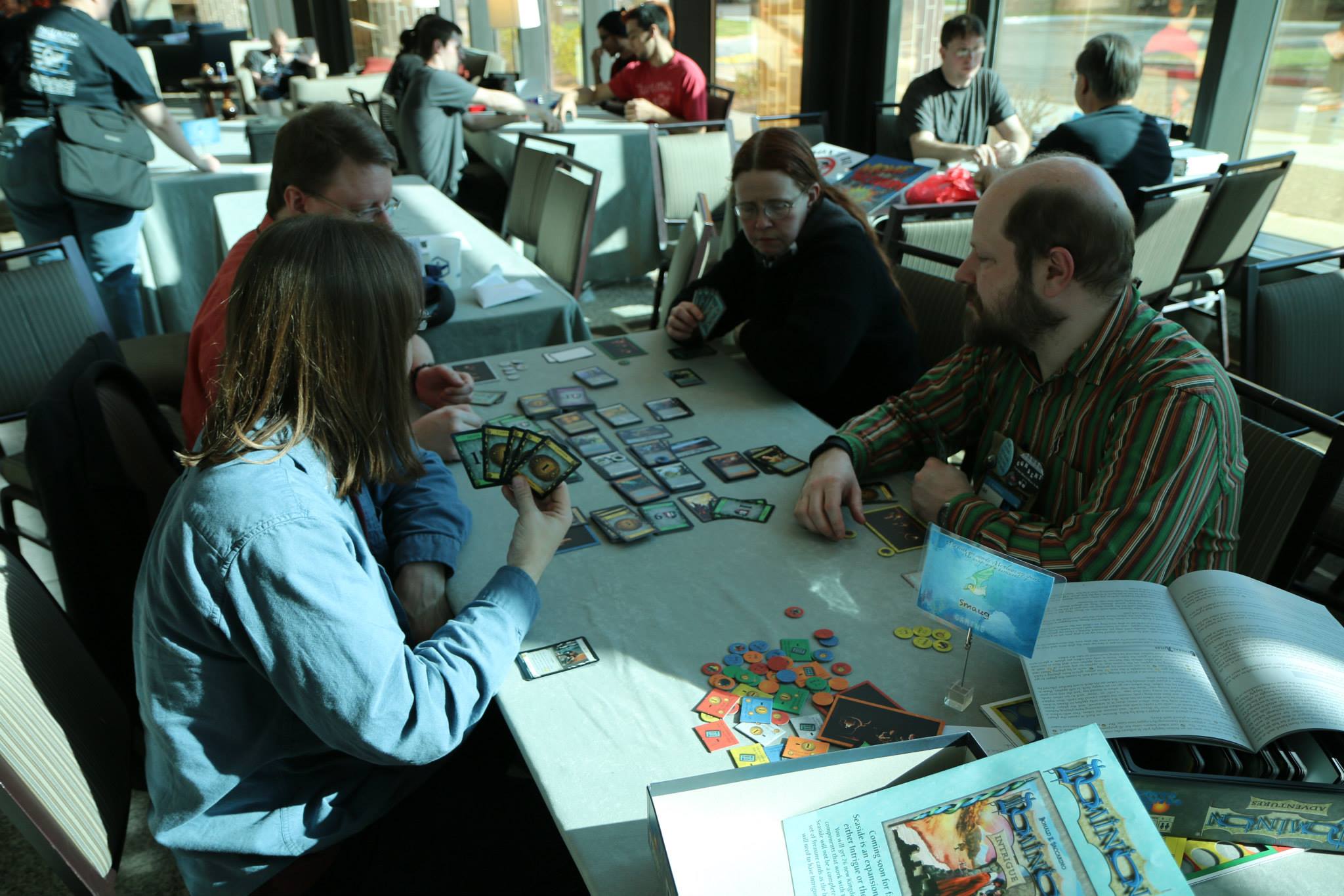 Group playing the deck building game Dominion with other groups in the background playing games