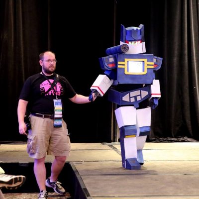 A volunteer holding the hand of a great transformers cosplayer as they walk the runway at the cosplay contest