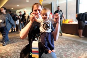 Penguicon-goer with tiny human who is wearing a Penguicon shirt